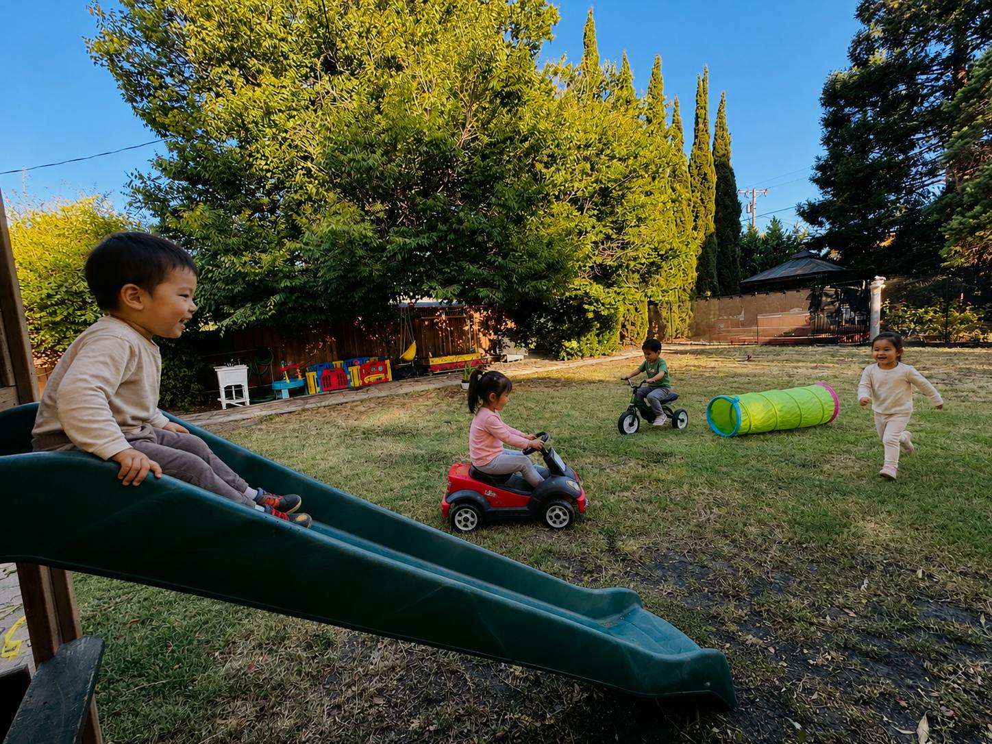 Child sitting on a green slide, child on a toy car, child on a tricycle, child running