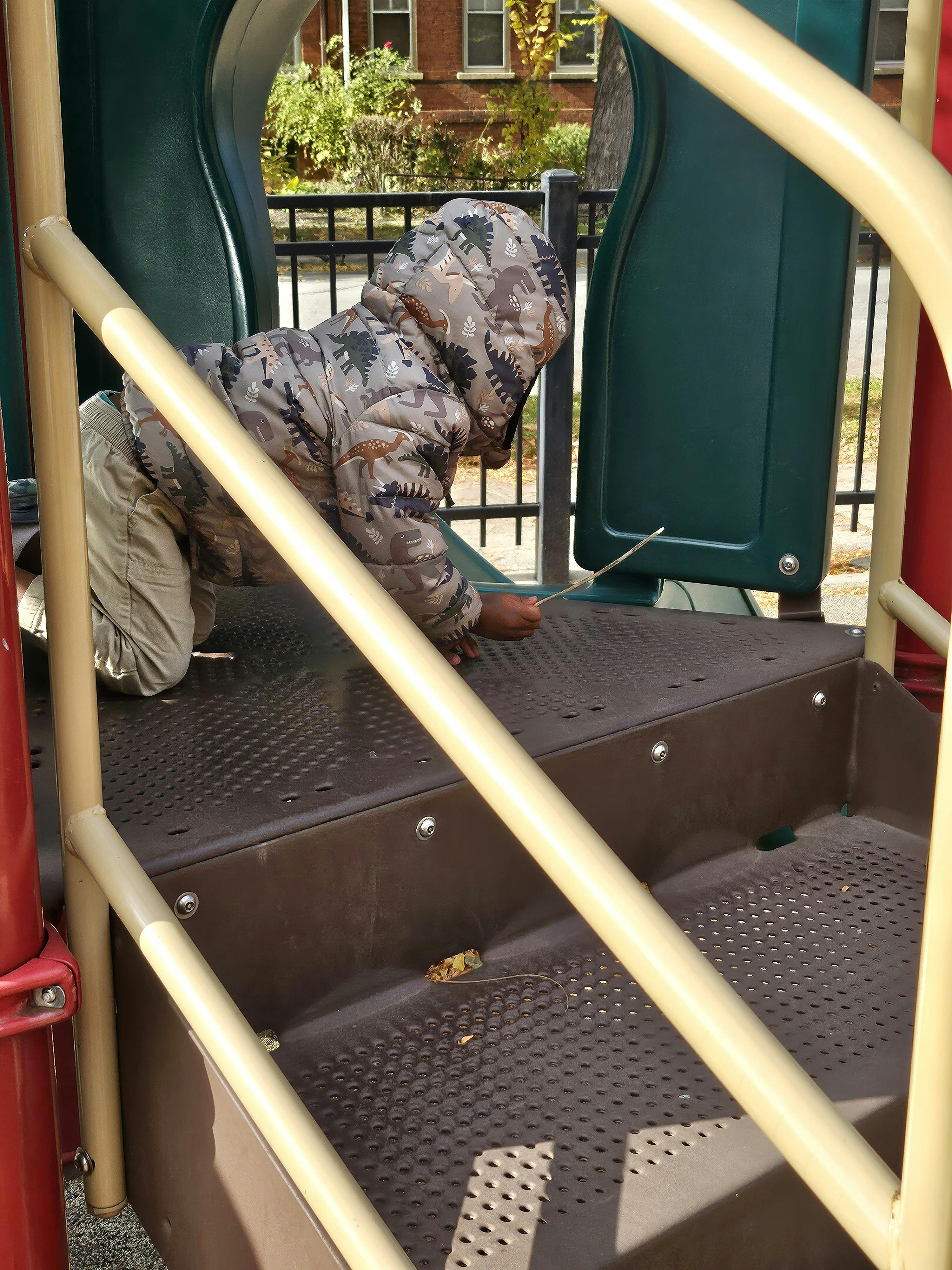 Child in a dinosaur jacket playing on a brown and green playground