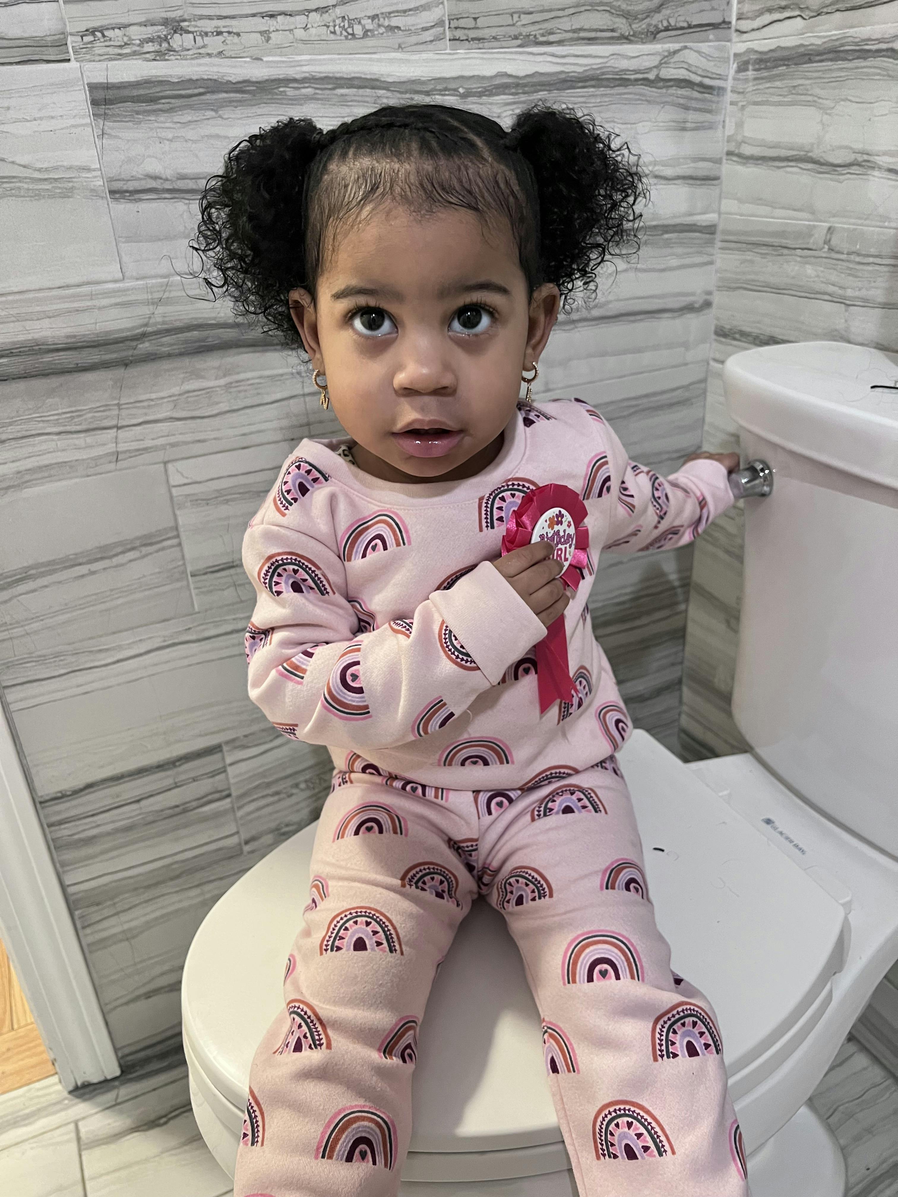 Child in rainbow pajamas sitting on a toilet