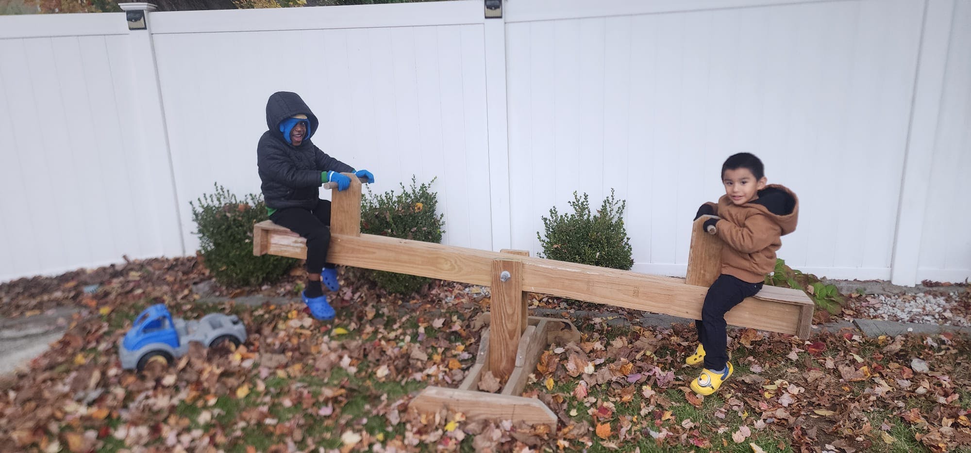 Two children on a wooden seesaw outdoors among fallen leaves