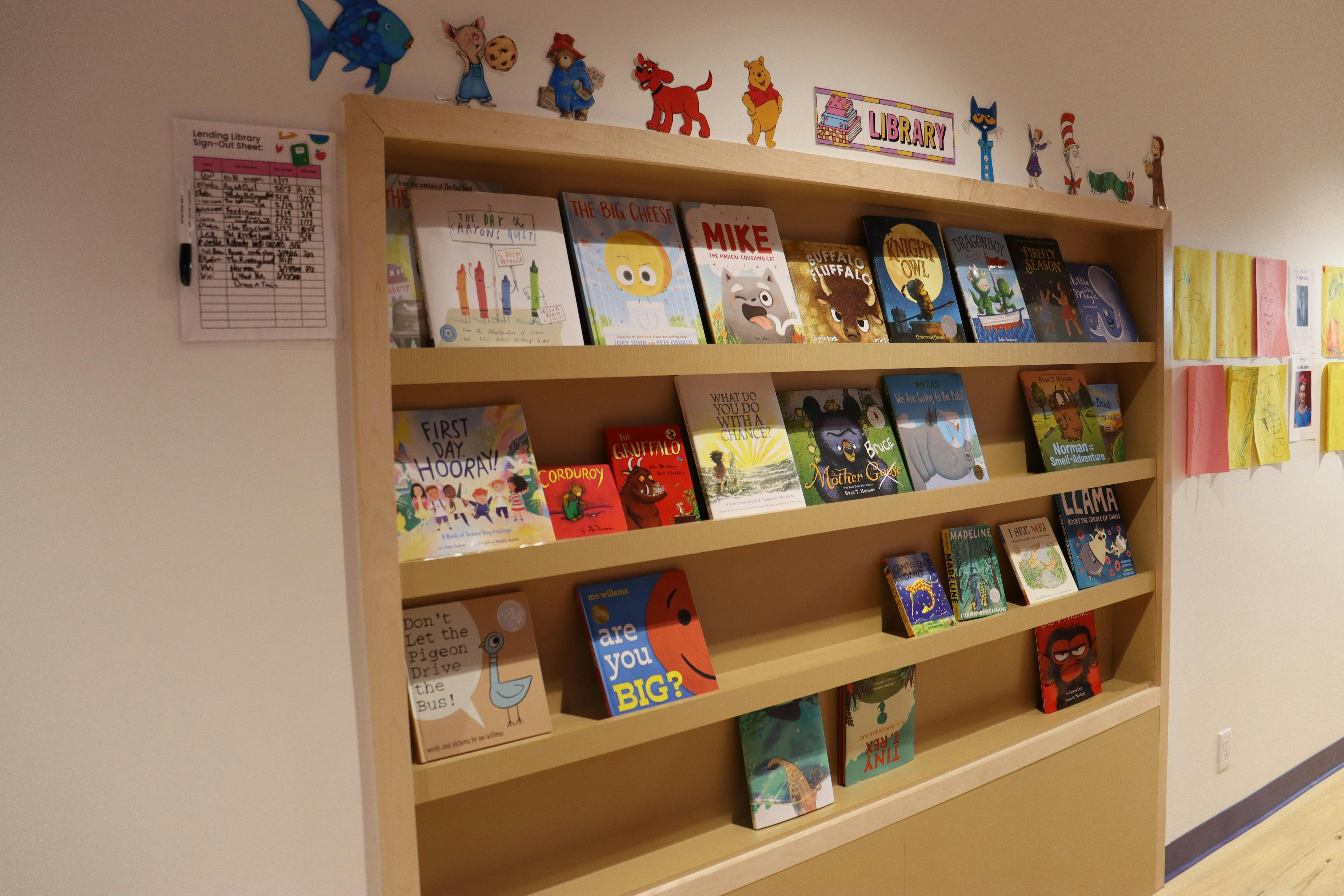 Children's books displayed on wooden shelves with cartoon character cutouts