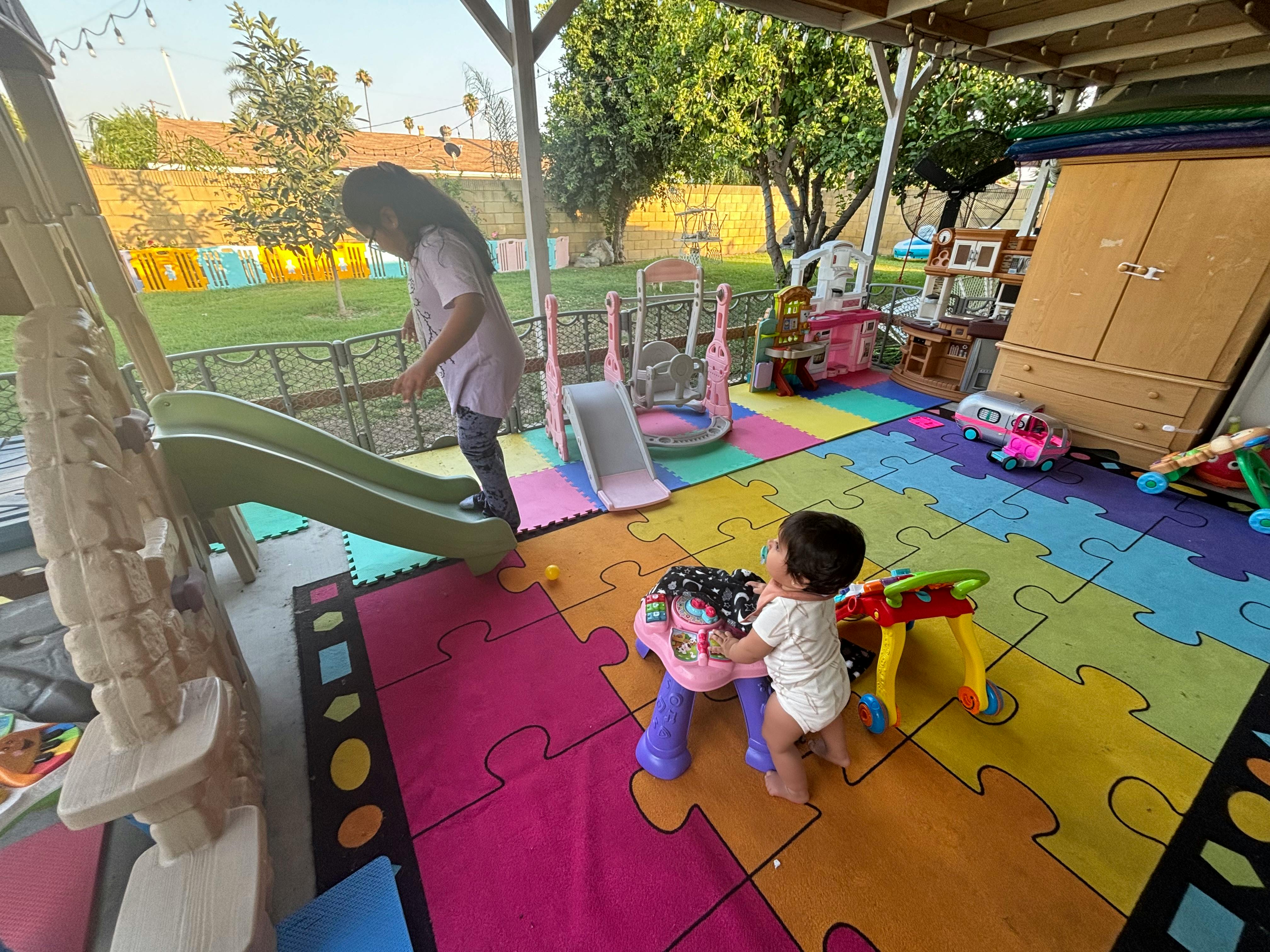 Child standing on a slide while a baby plays with a toy on a colorful mat