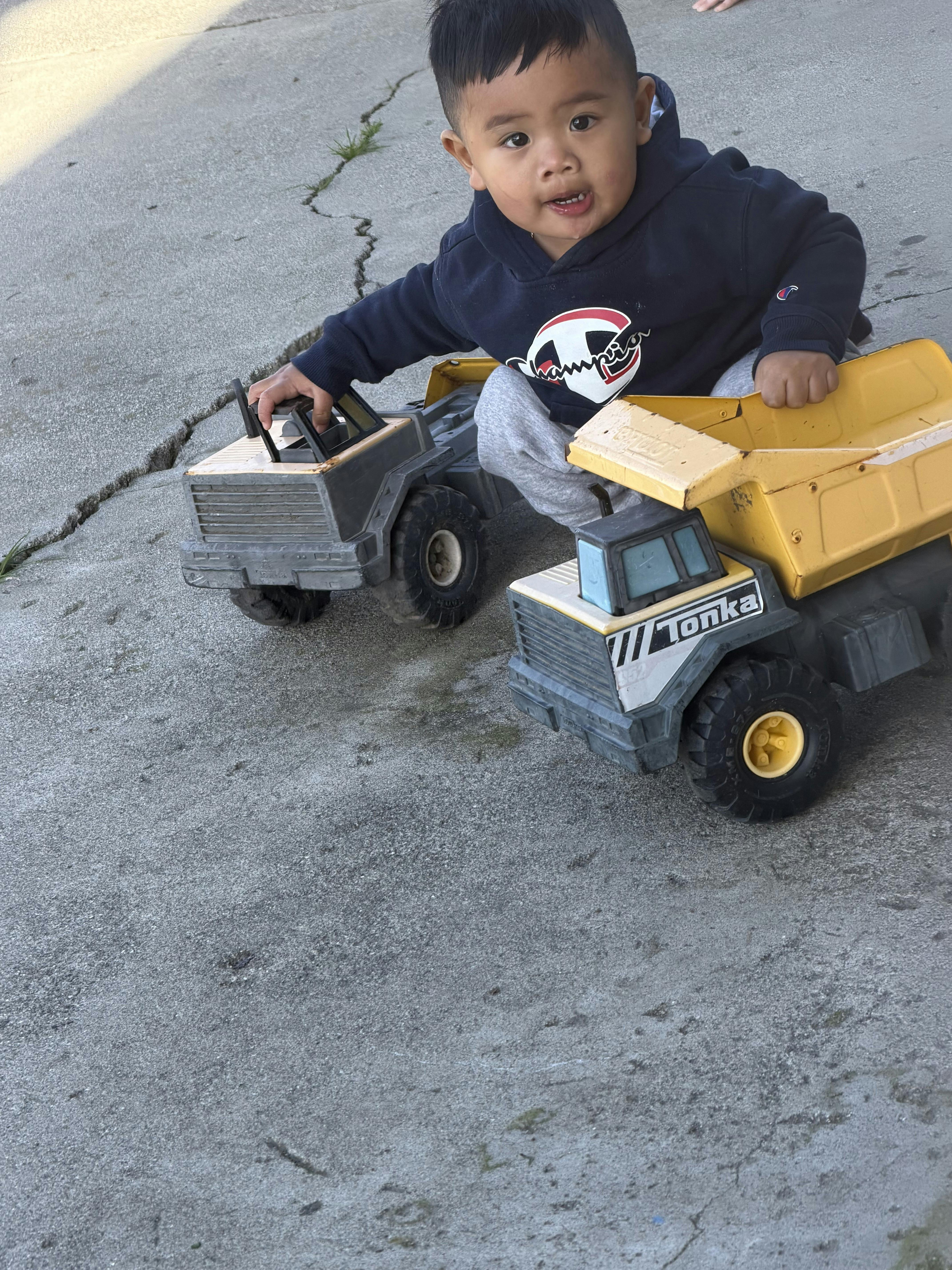 Child playing with two toy dump trucks outdoors