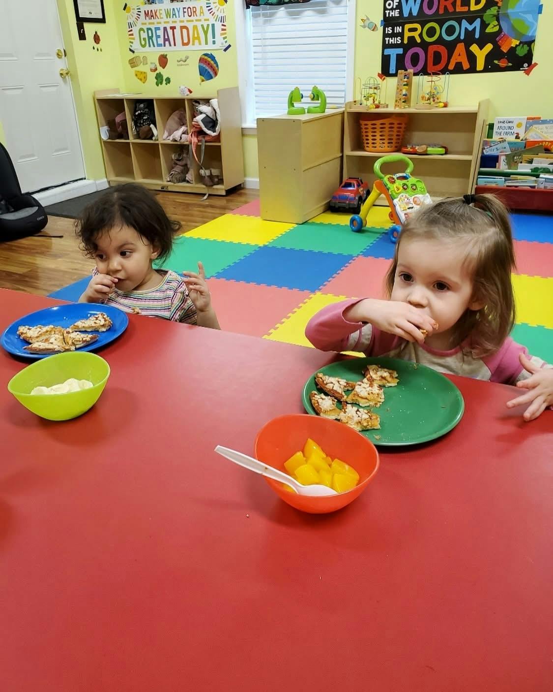 Two children sitting at a red table eating snacks in a classroom