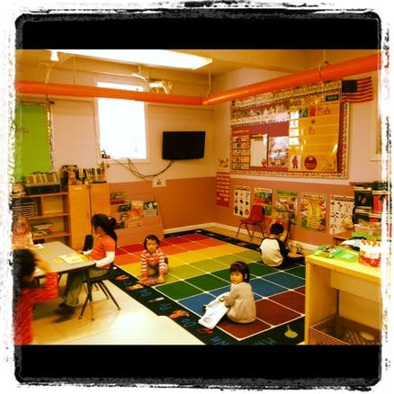 Children in a classroom, some sitting at a table, others on a colorful rug