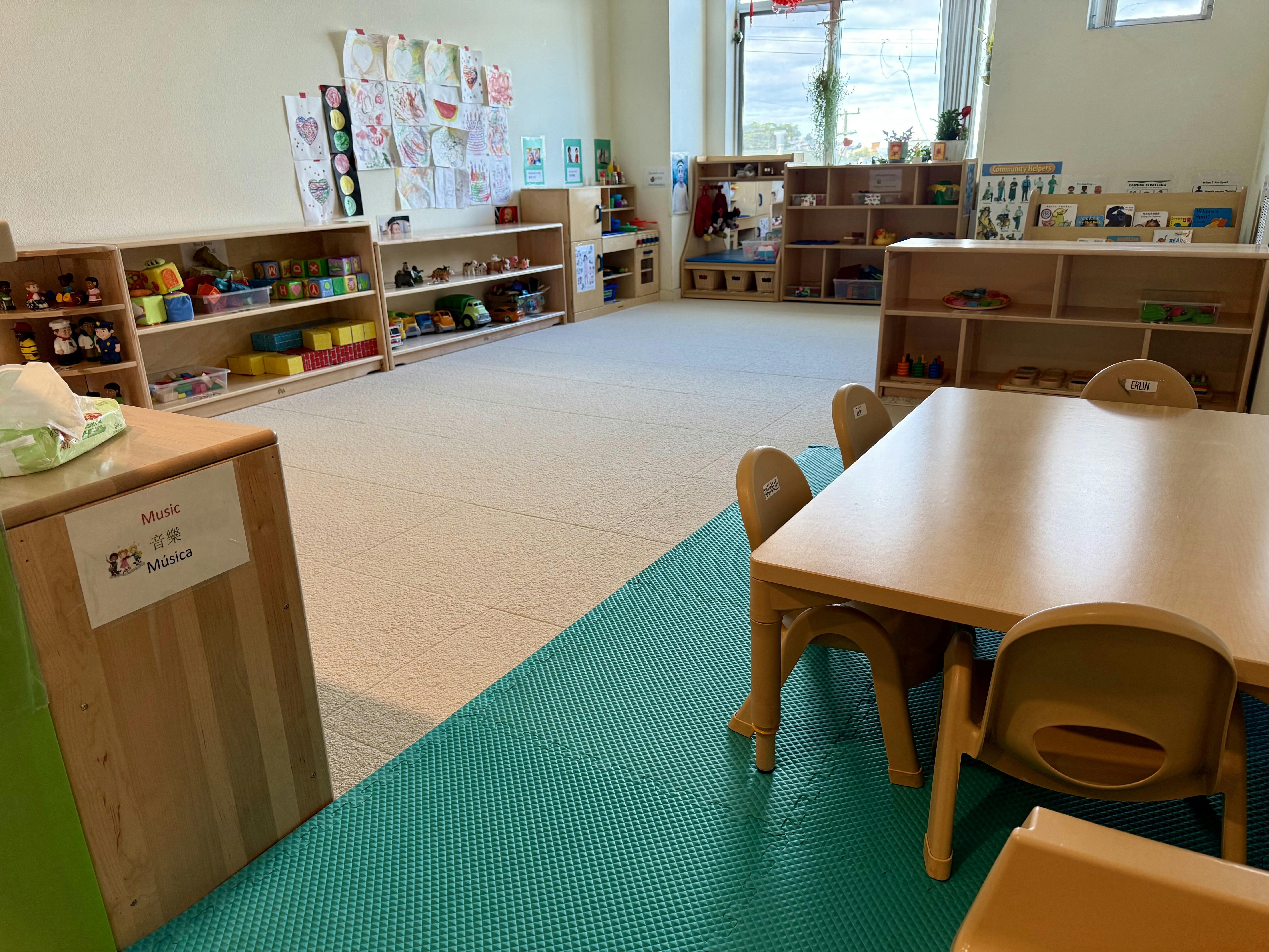 Classroom with shelves of toys, children's artwork on walls, and a small table with chairs