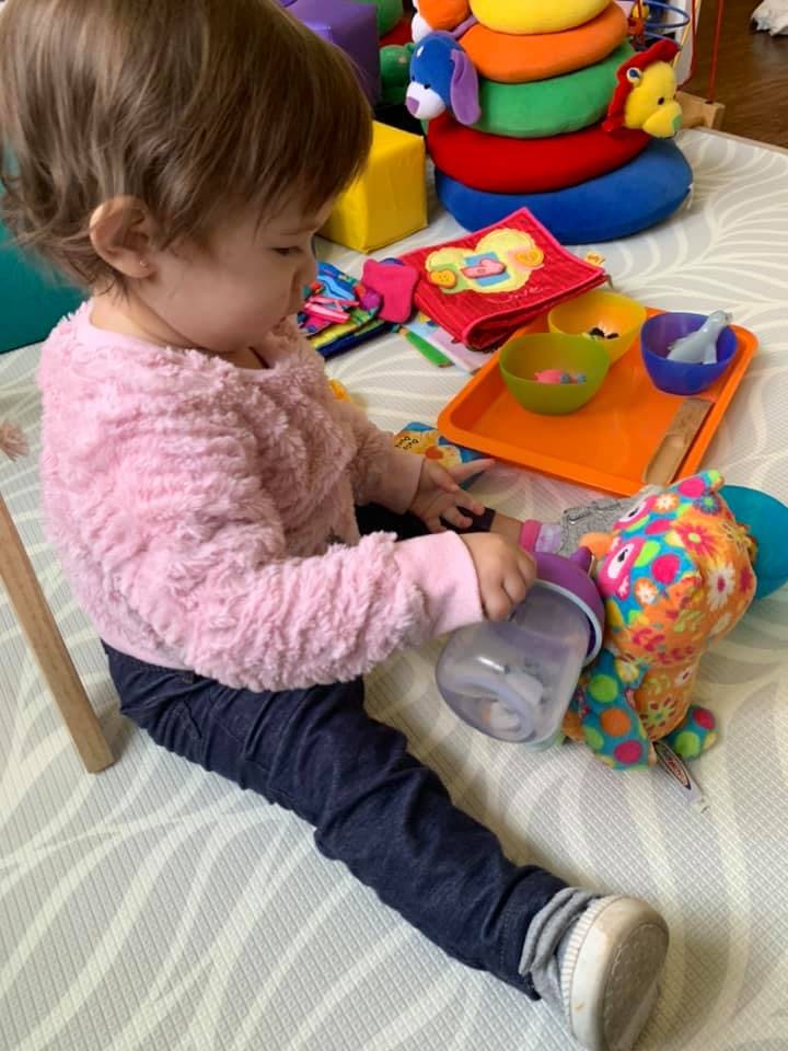 Child playing with a bottle and a colorful stuffed animal