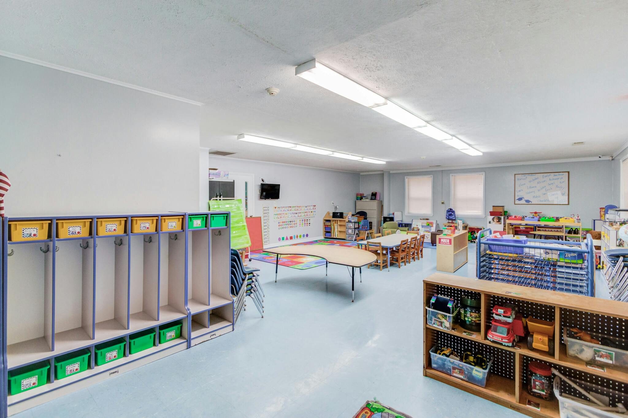 An empty preschool classroom with cubbies, tables, and toys