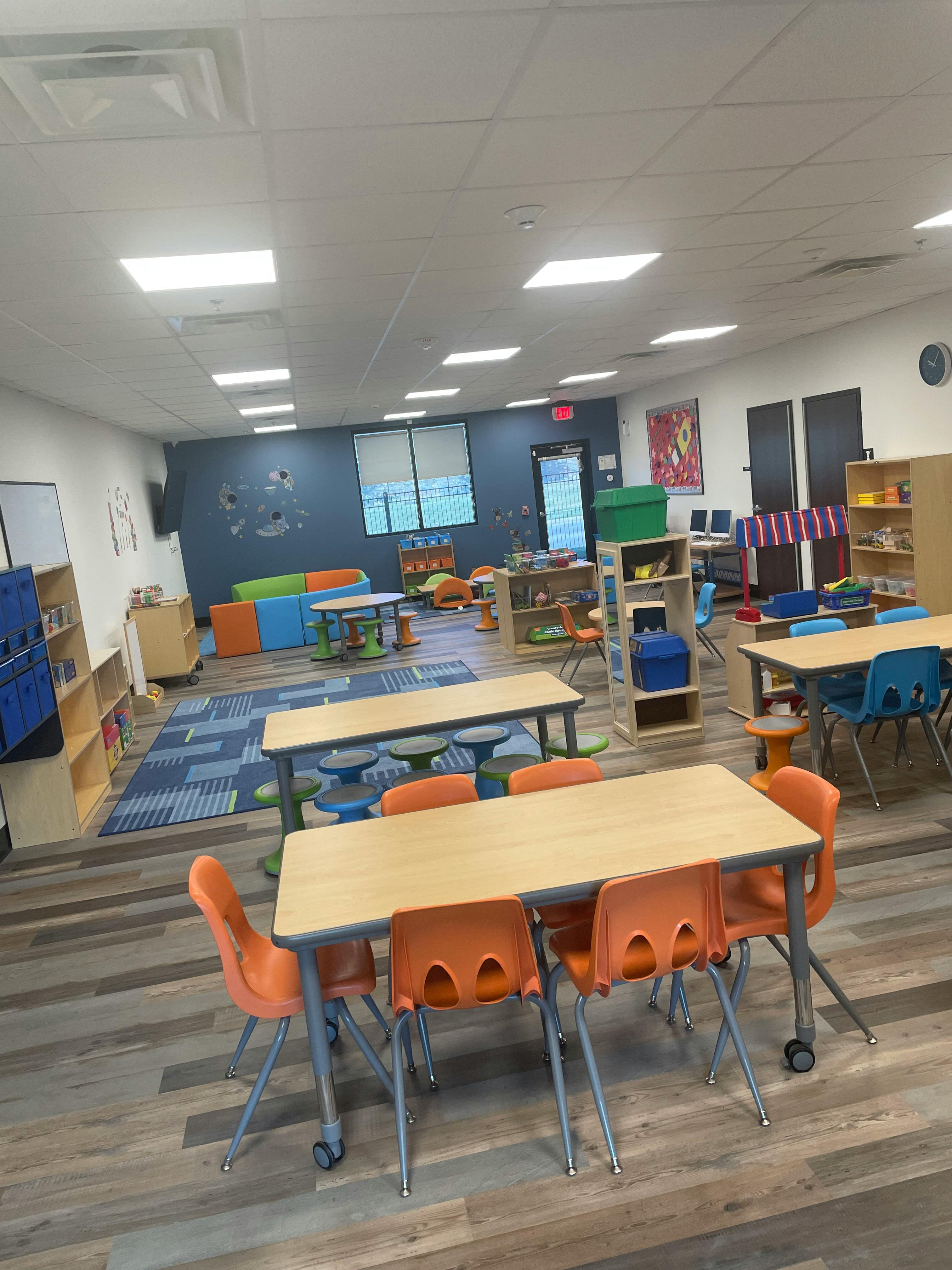 Classroom with tables and chairs, blue rug, and shelves