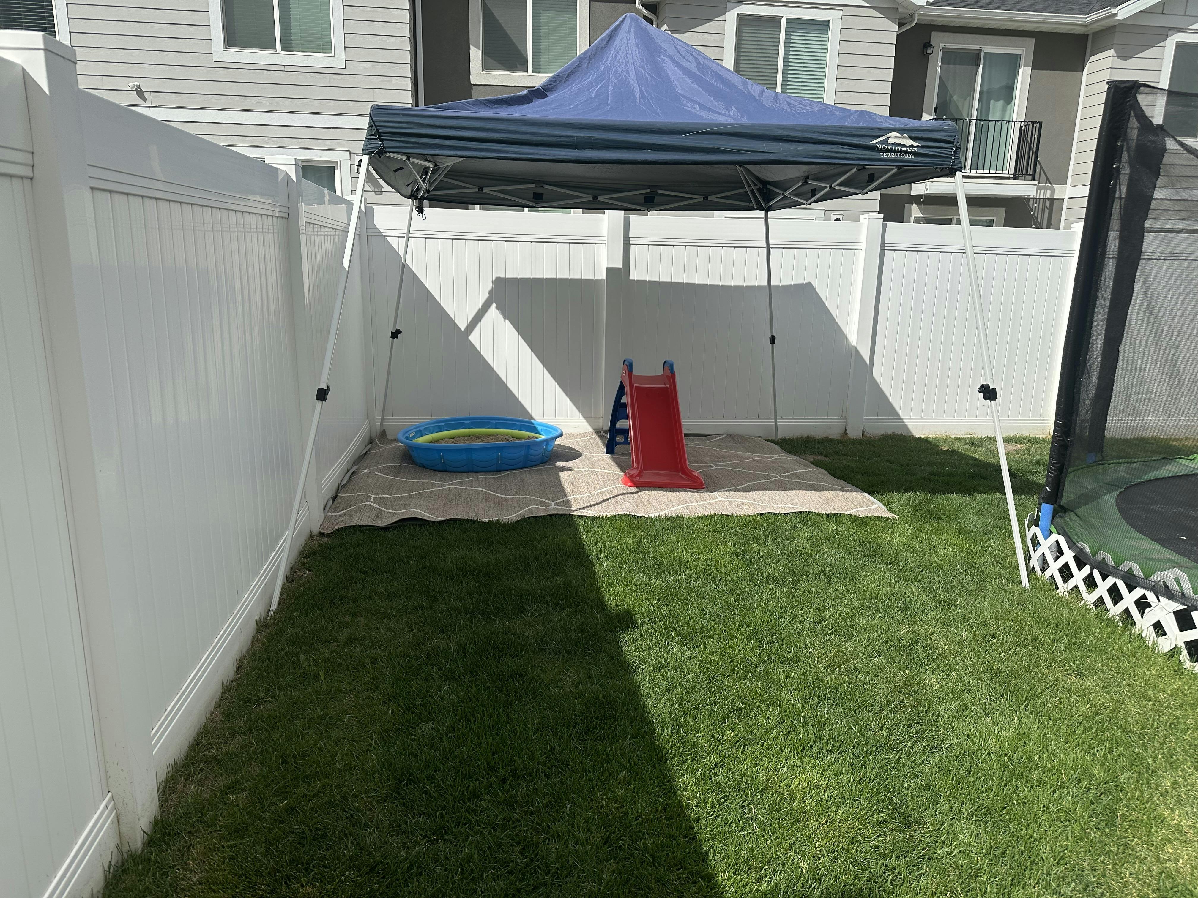 Blue canopy tent over a kiddie pool and red slide in a grassy backyard
