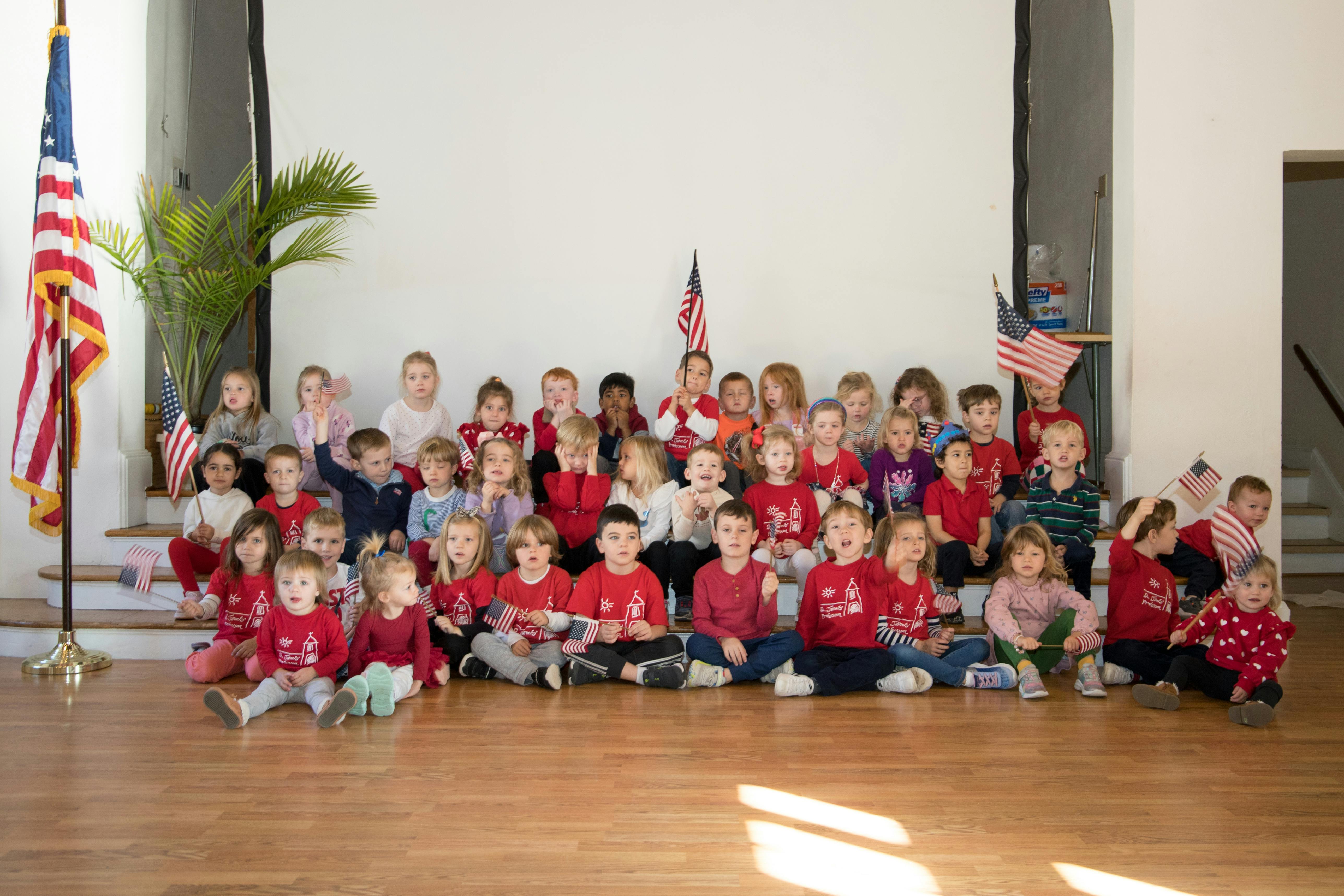 Group of children sitting on the floor and steps with American flags