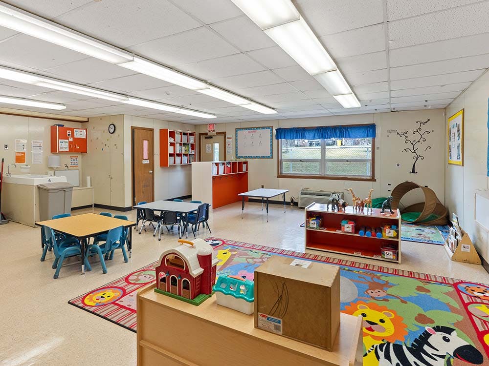 Empty preschool classroom with small tables, chairs, and colorful rug