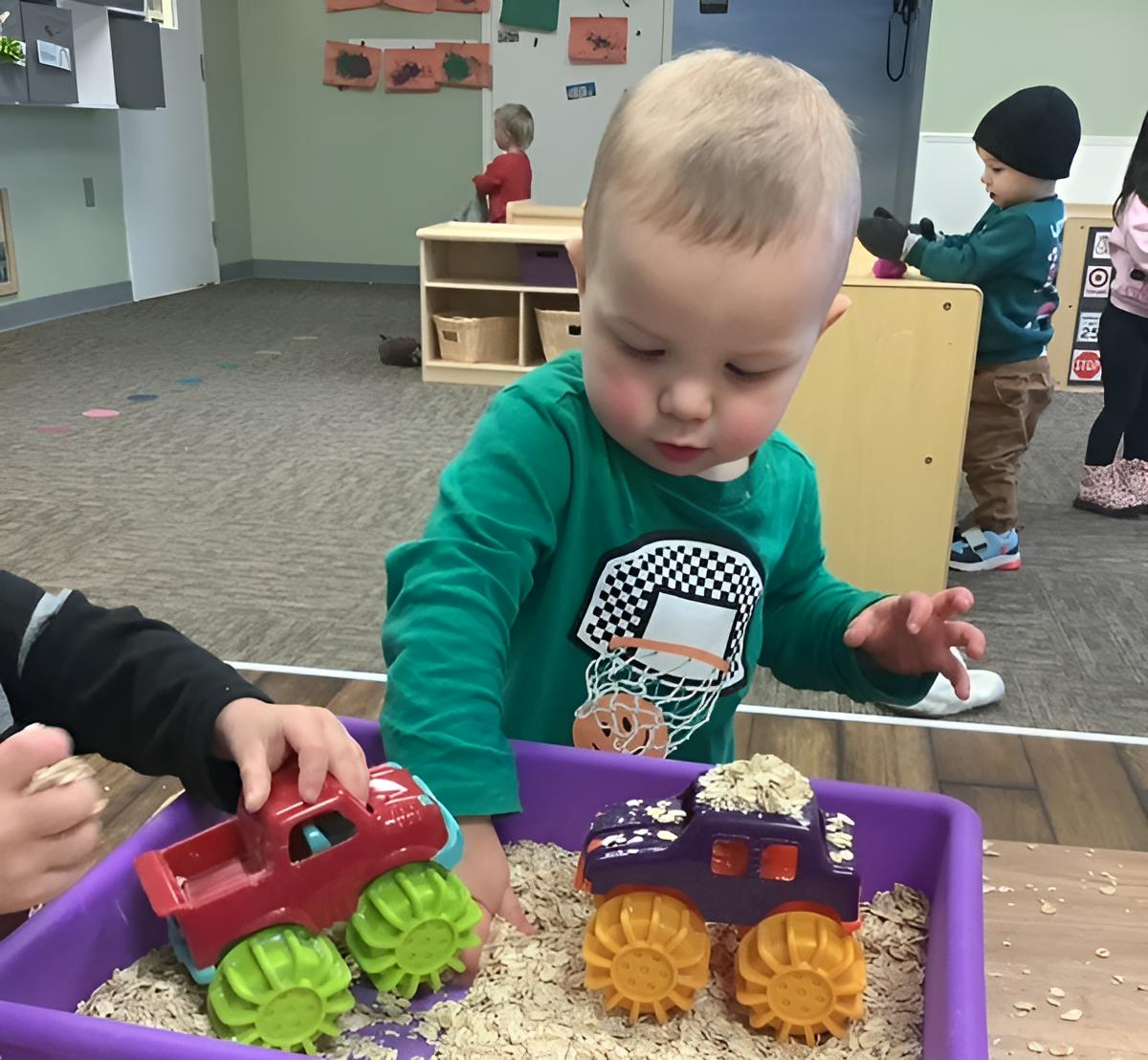 Child playing with toy monster trucks in a sensory bin