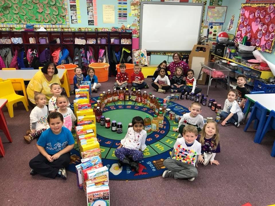 Adult and children sitting on a rug with food donations in a classroom