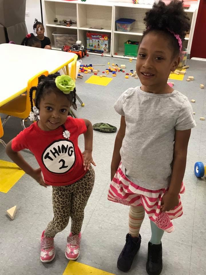 Two children standing in a room, one wearing a red shirt with "Thing 2"
