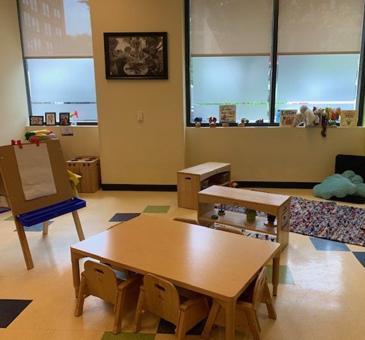 Classroom with small tables and chairs, an easel, and windows