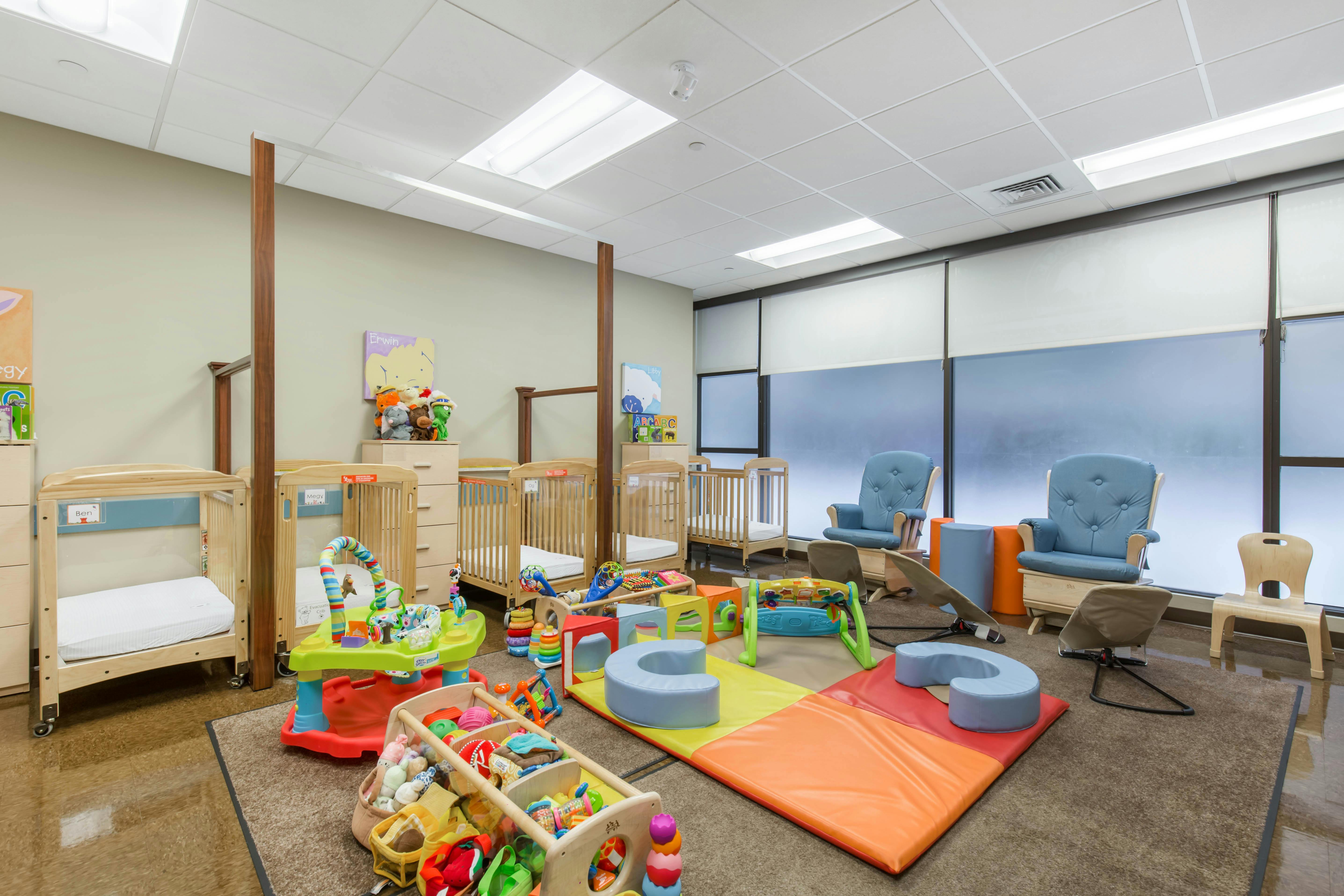 A colorful childcare room with cribs, play mats, and toys