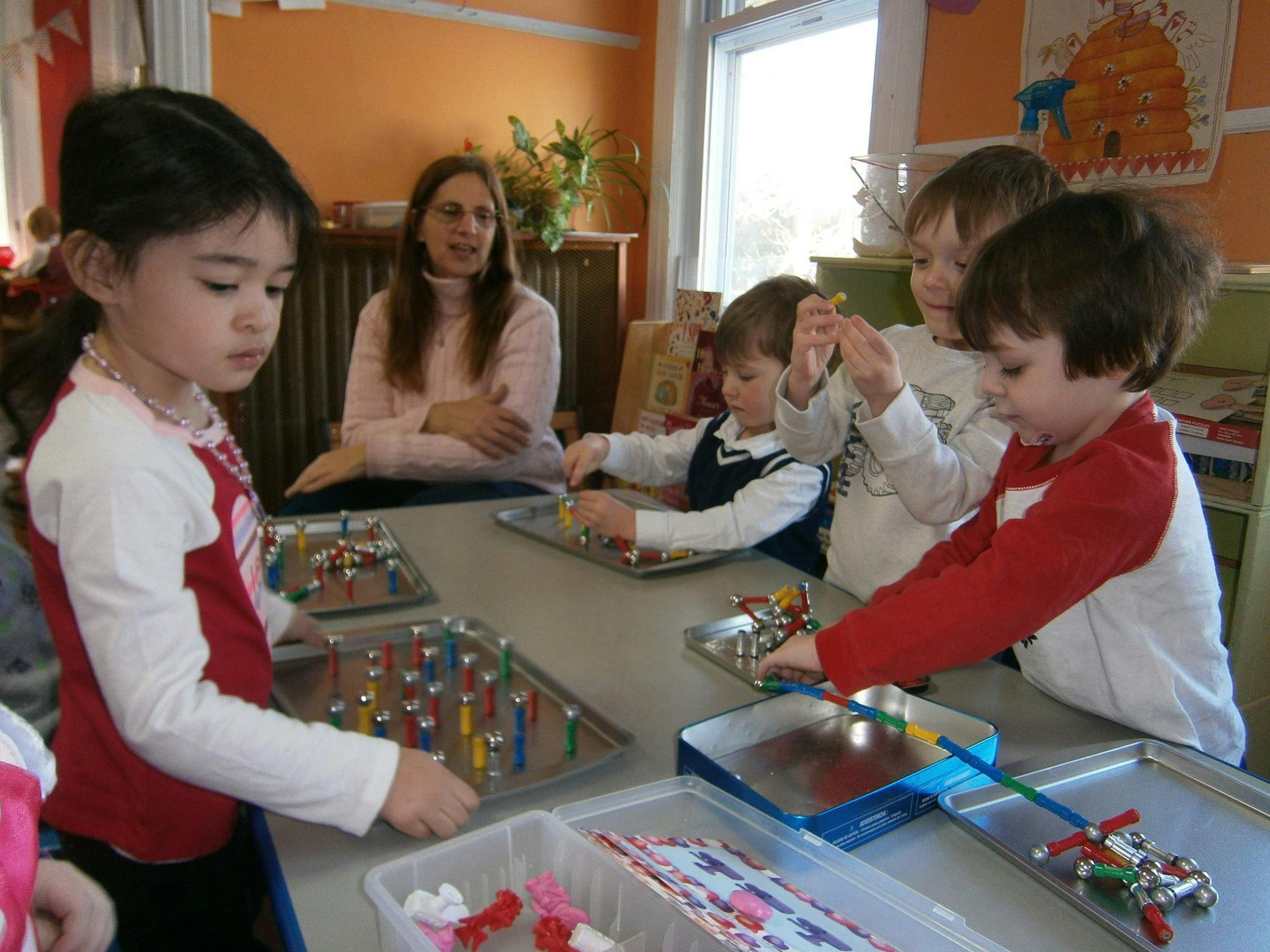Children and an adult at a table with trays of small objects