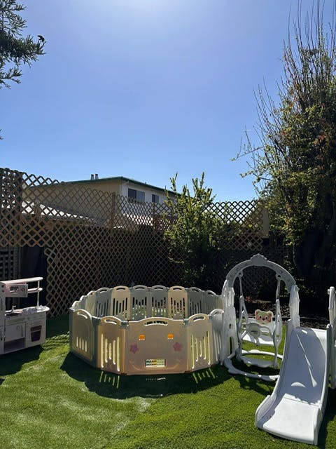 Outdoor play area with a playpen, slide, and swing set on grass