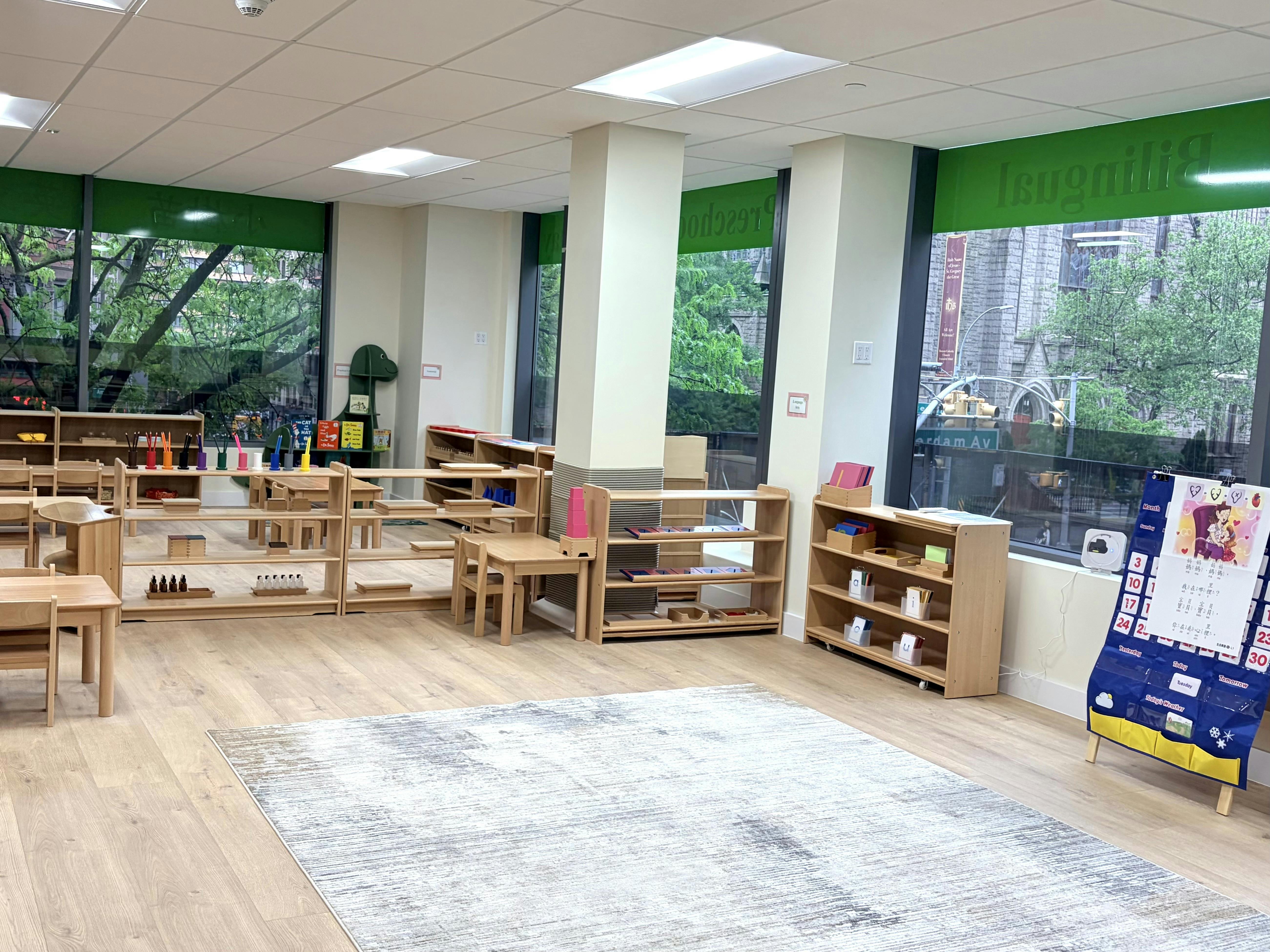 Classroom with wooden furniture, shelves with learning materials, and large windows