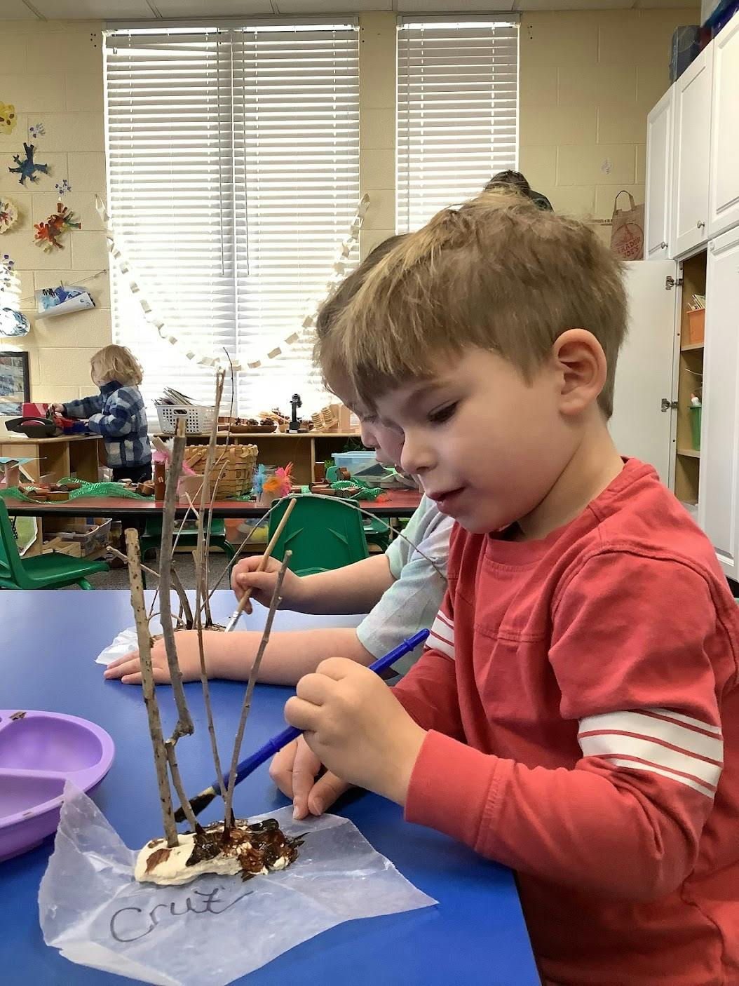 Children painting sticks attached to clay in a classroom