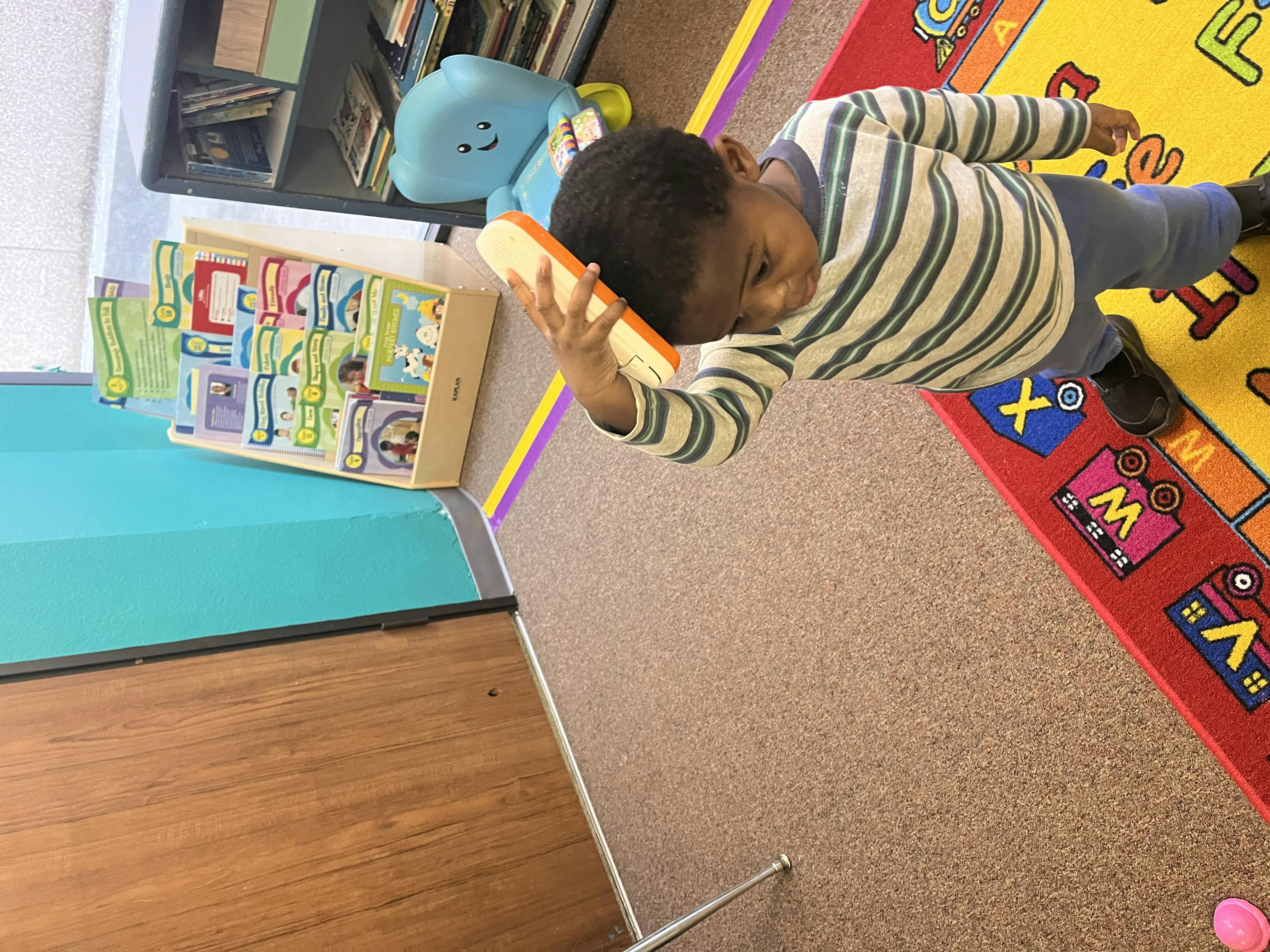 Child holding a toy phone to their ear in a classroom