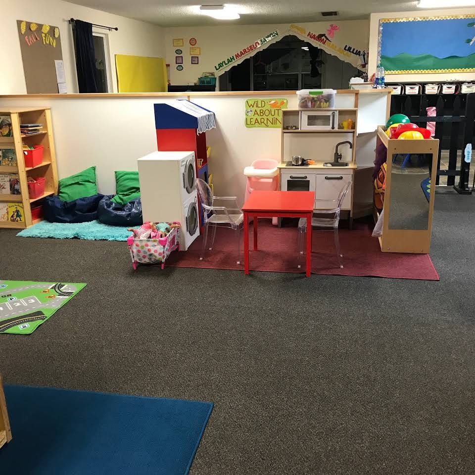 Play area with toy kitchen, red table, and bean bags in a classroom
