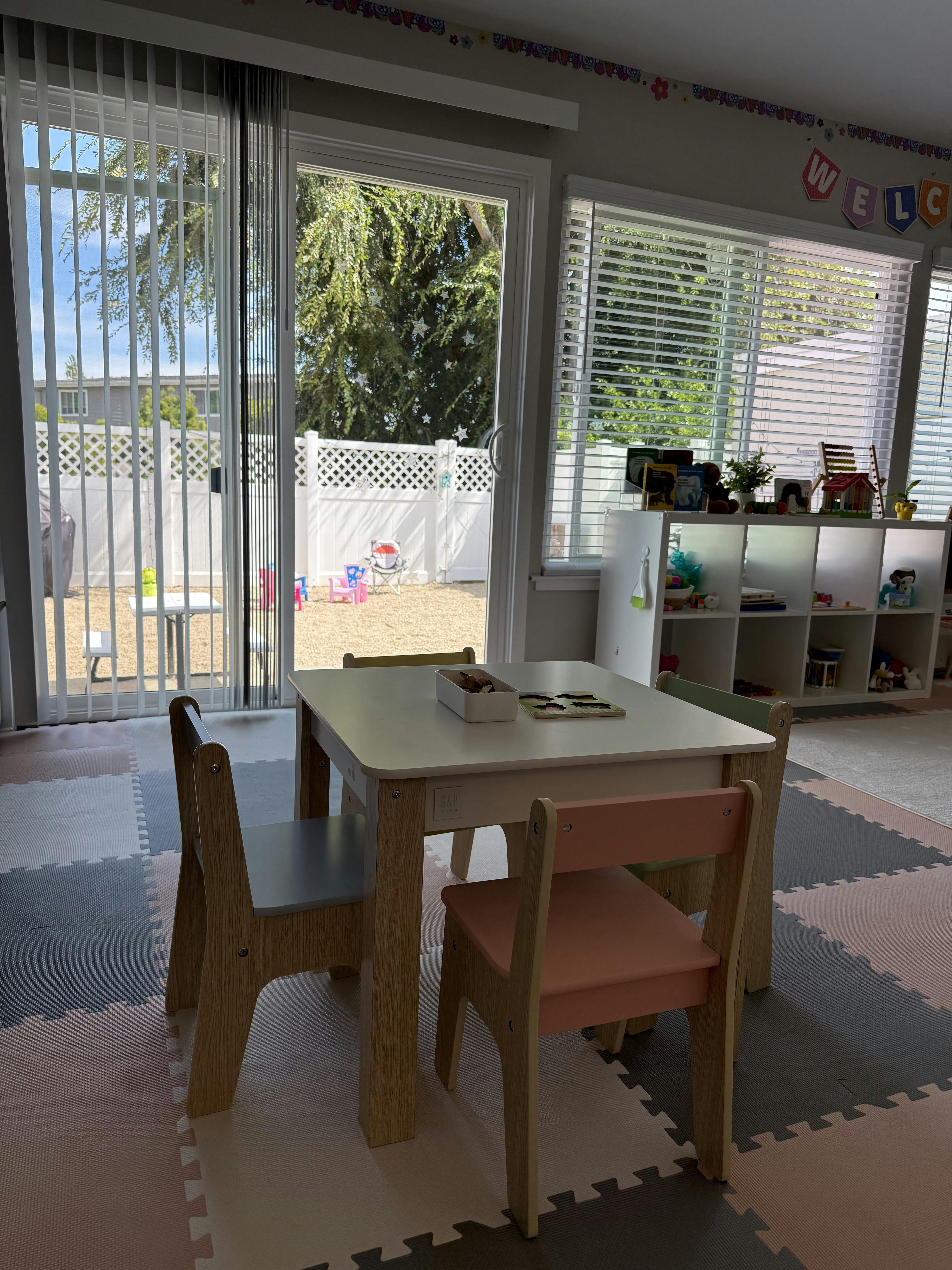 Child-sized table and chairs in a playroom with a view of a backyard