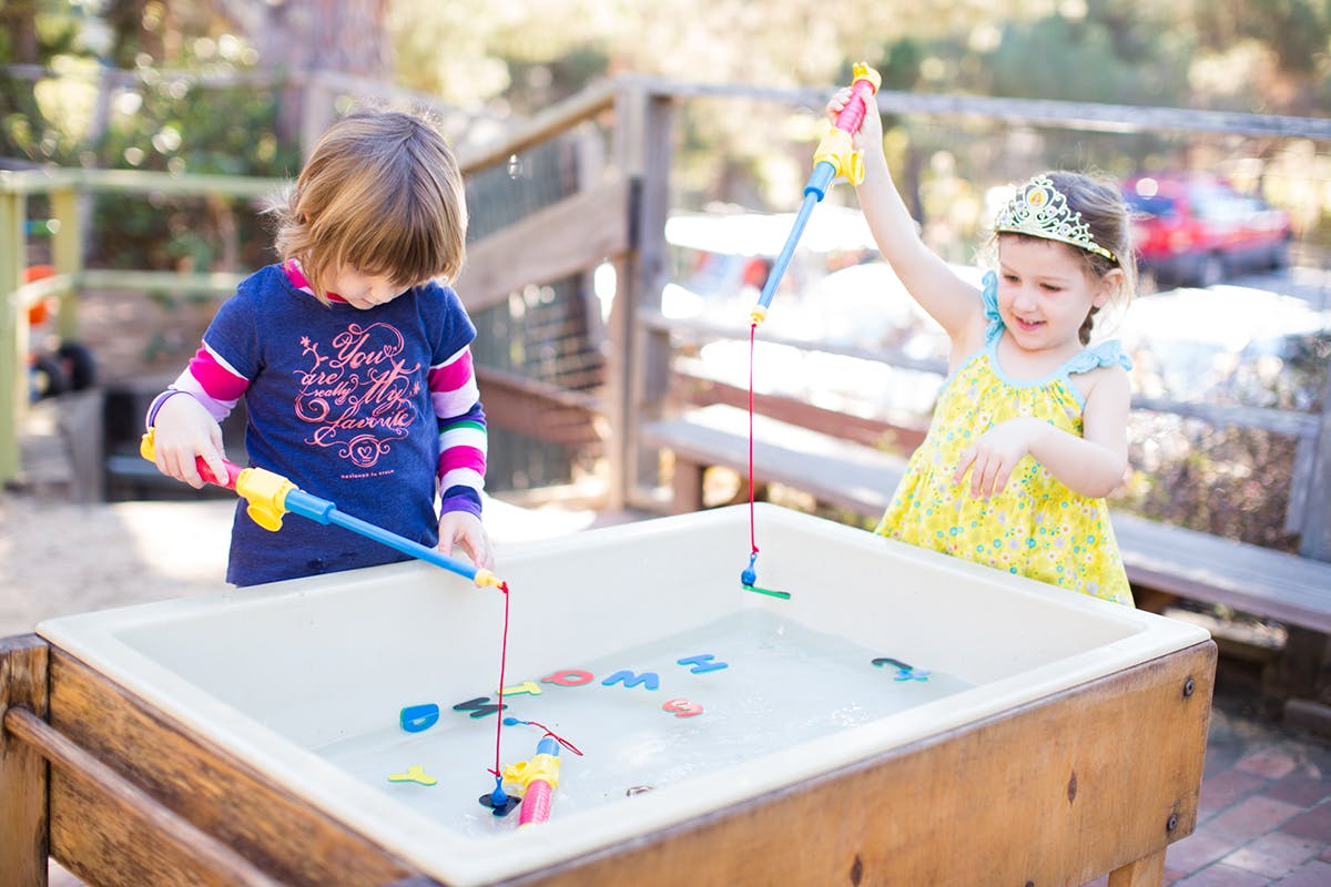 Two children playing with fishing rods in a water table