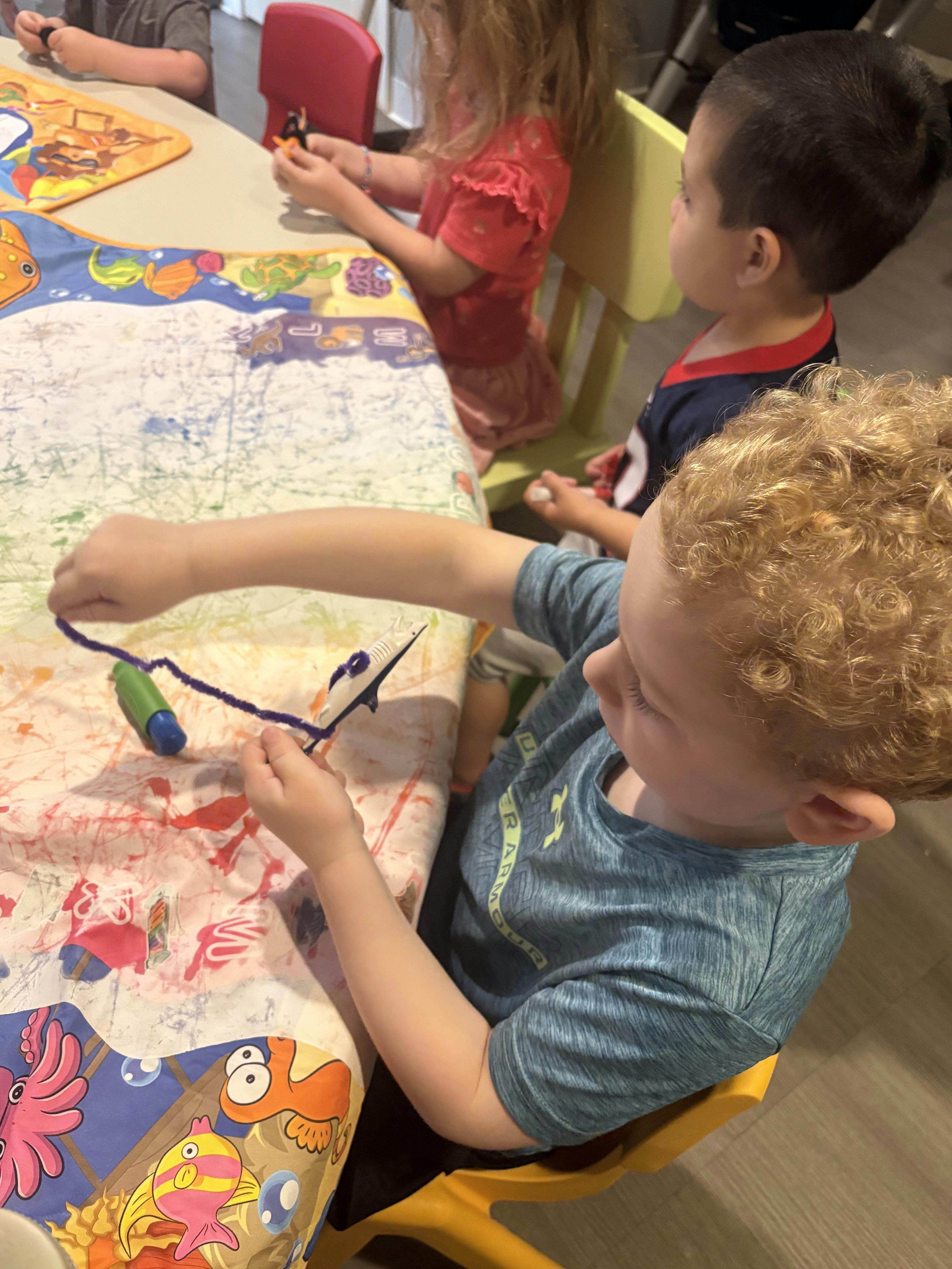 Children sitting at a table crafting with pipe cleaners