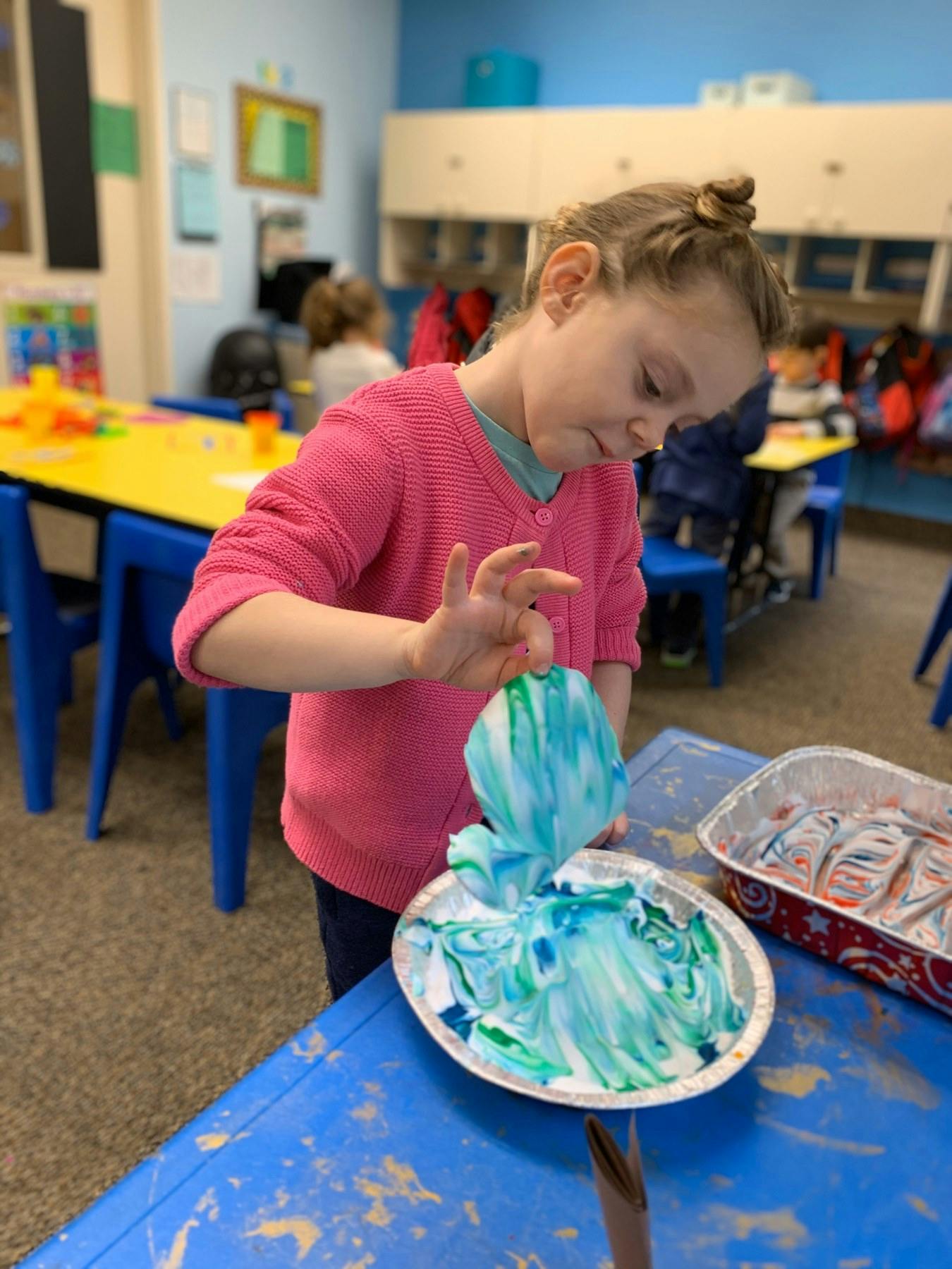 Child creating art with blue and green paint in a classroom