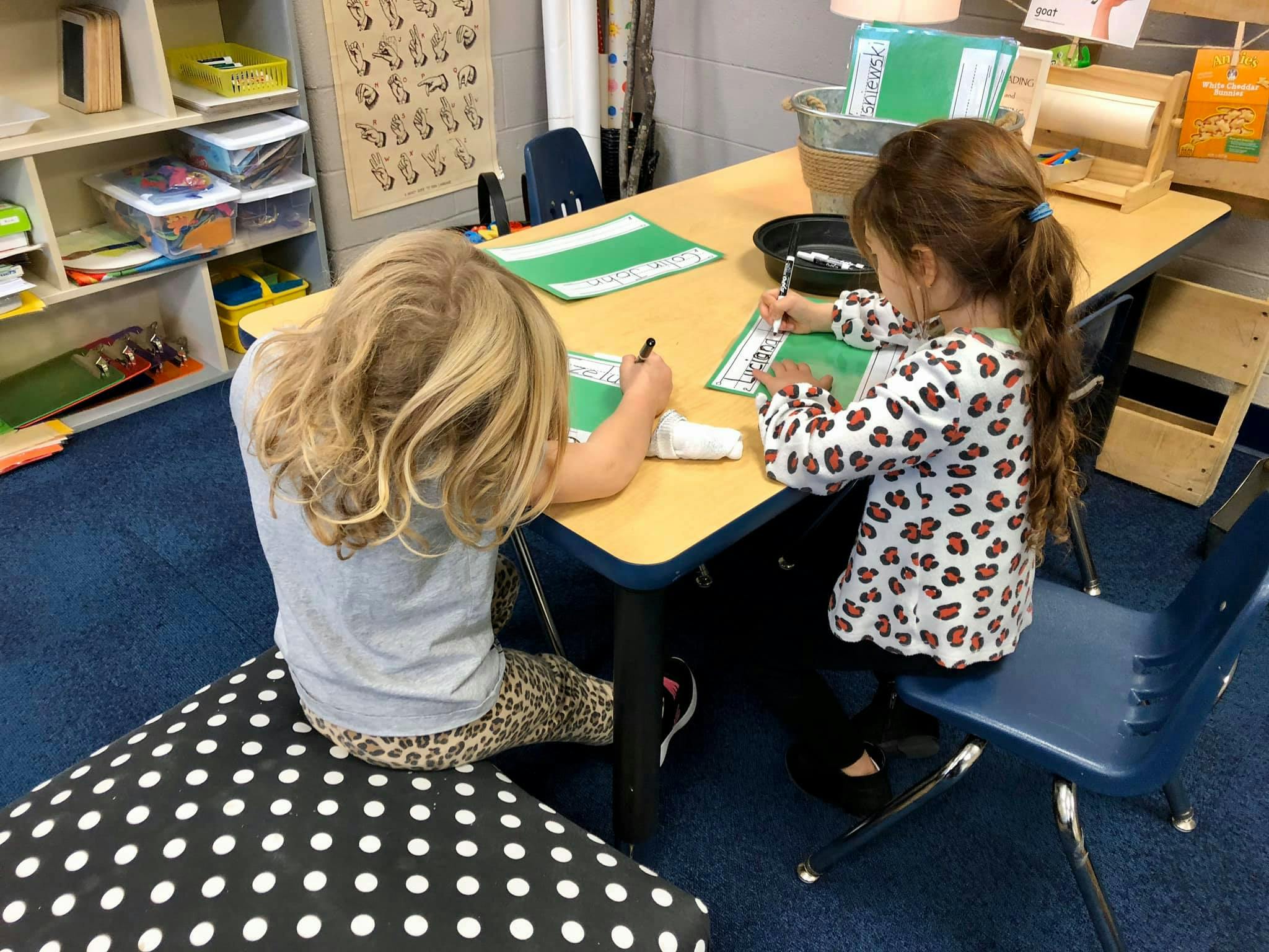 Two children writing at a table in a classroom