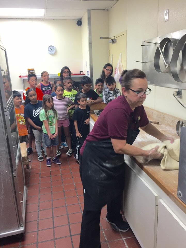 Person in apron kneading dough with children watching in a kitchen