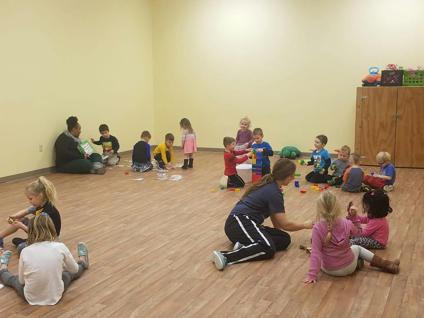 Adults and children sitting on the floor playing with toys