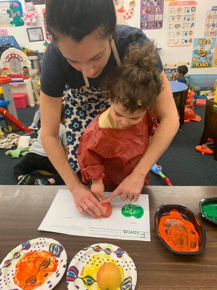 Adult and child doing apple printing art in a classroom