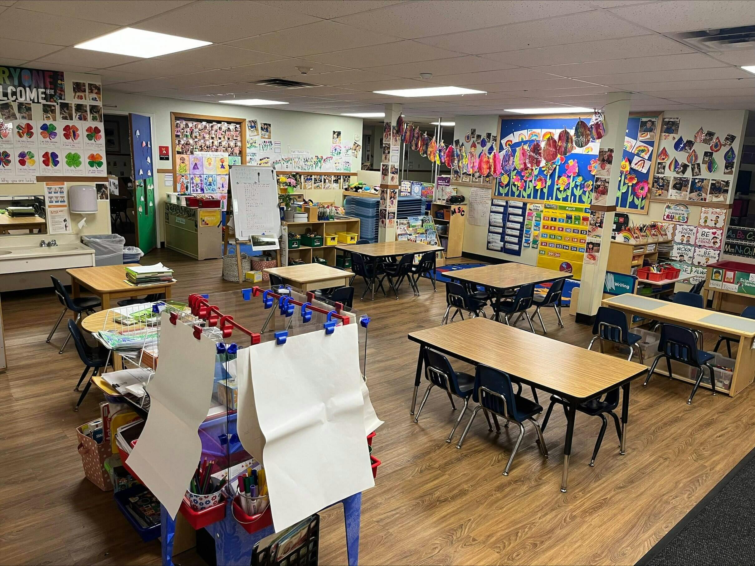 Empty classroom with small tables and chairs, decorated with children's artwork