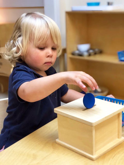Child playing with a wooden box and blue disc
