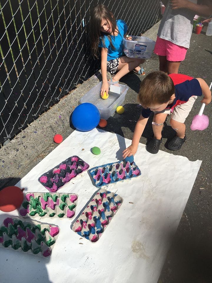 Children painting egg cartons on a white sheet outdoors