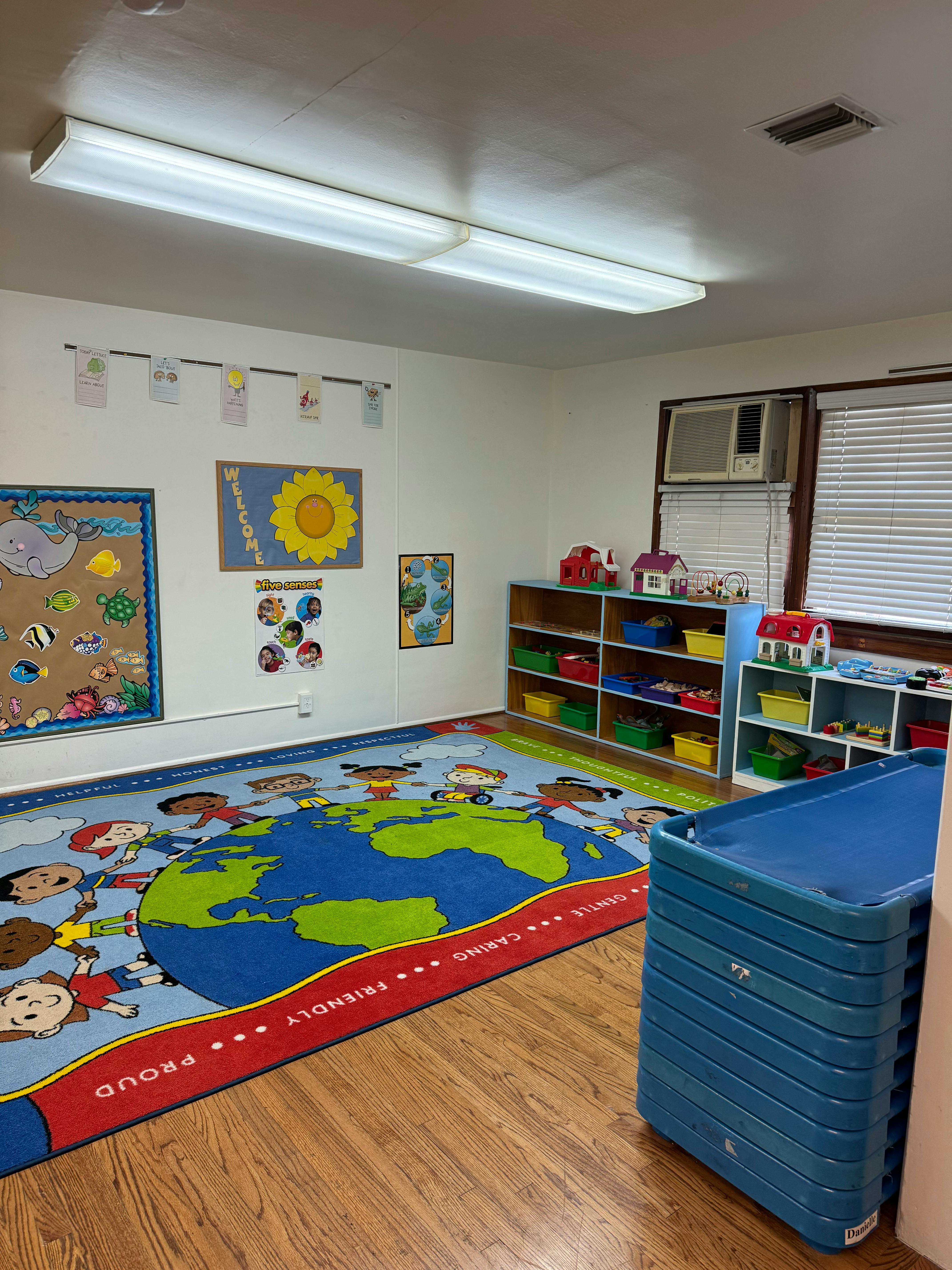 Classroom with a world map rug, shelves with toys, and wall decorations