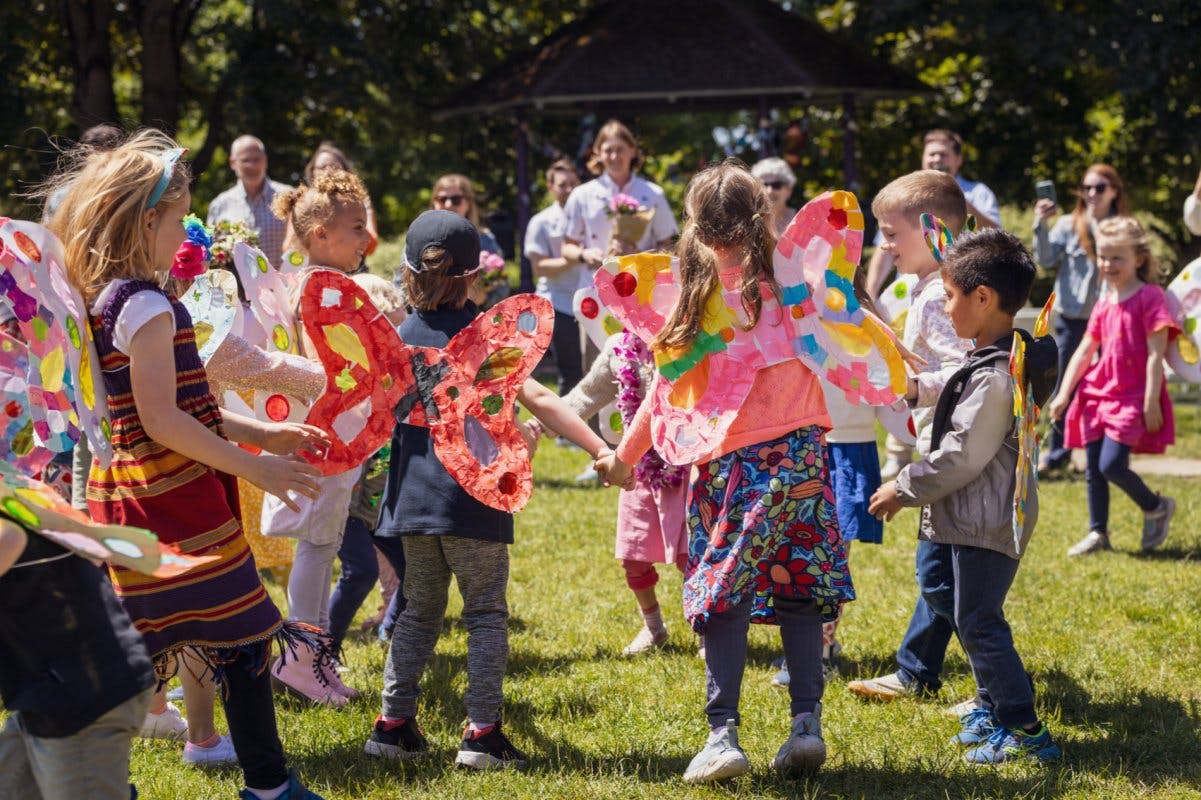Children wearing butterfly wings holding hands in a circle on grass