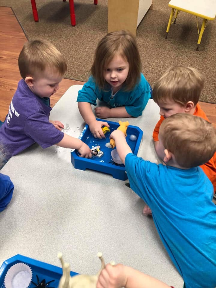 Four children playing with toys in a blue tray