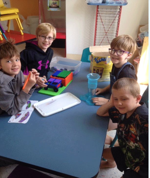 Four children sitting at a table with toys and craft supplies