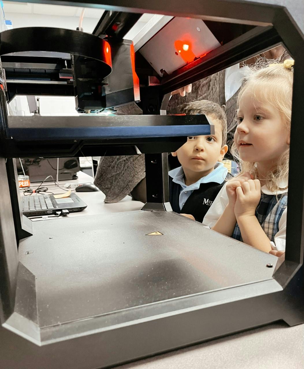 Two children looking into a machine with red lights