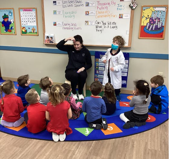 Adult and child in lab coat presenting to a group of children in a classroom