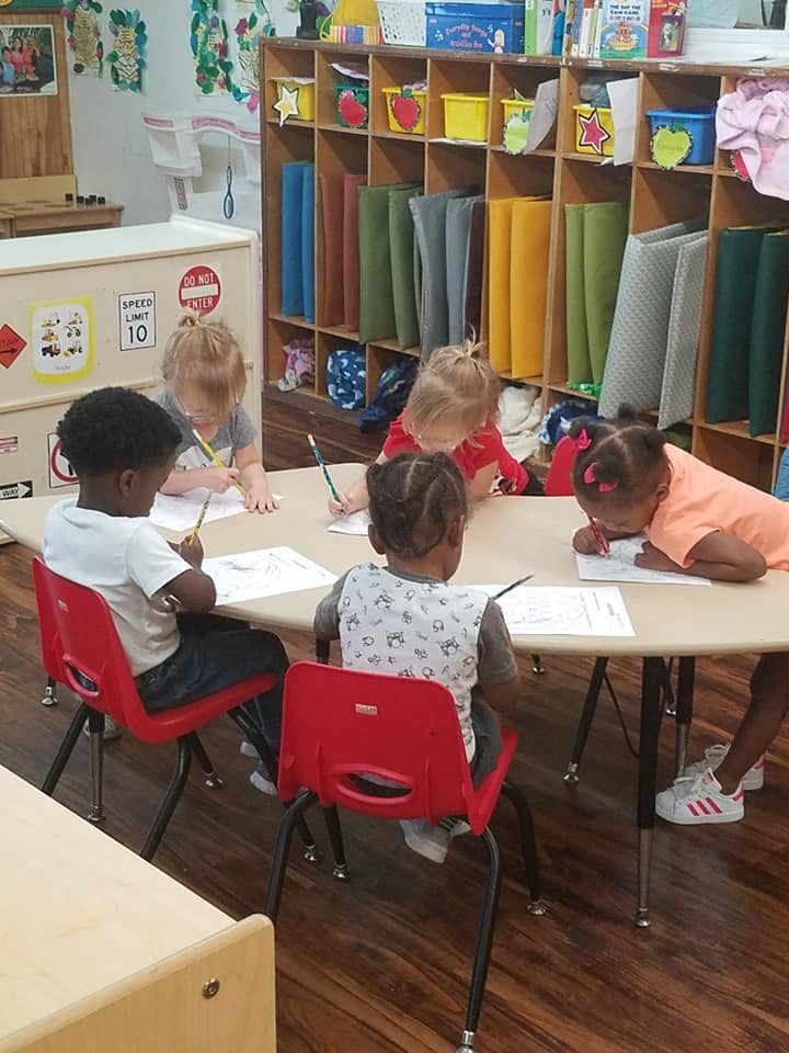 Children sitting at a table drawing in a classroom