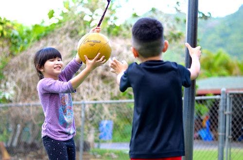 Child holding a tetherball while another child stands by a pole