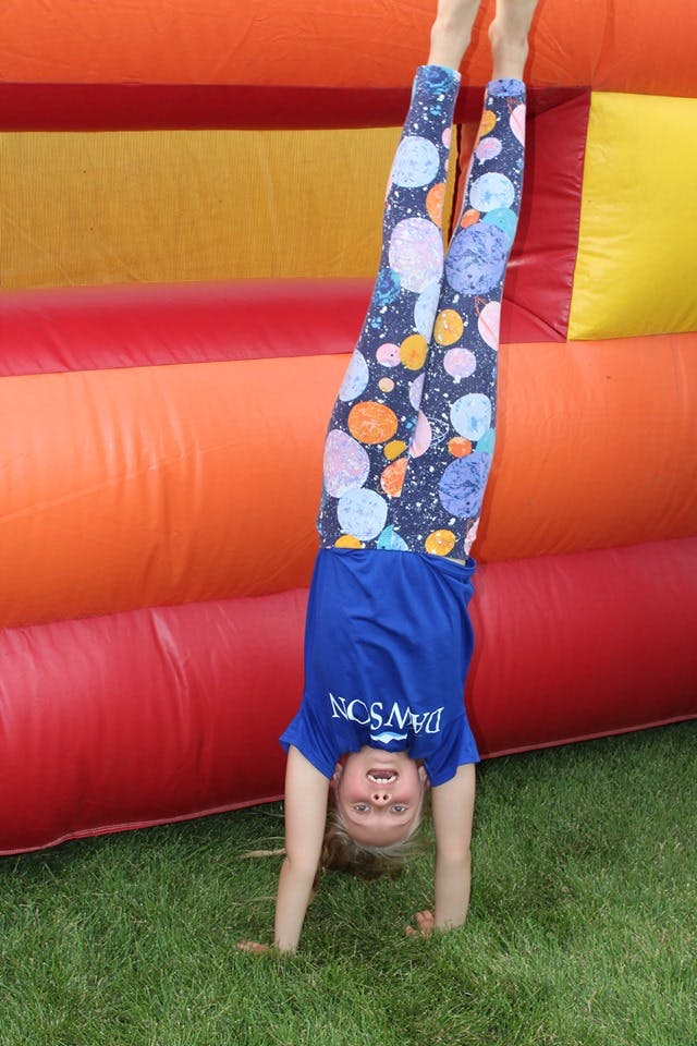 Child doing a handstand on grass next to an inflatable bounce house