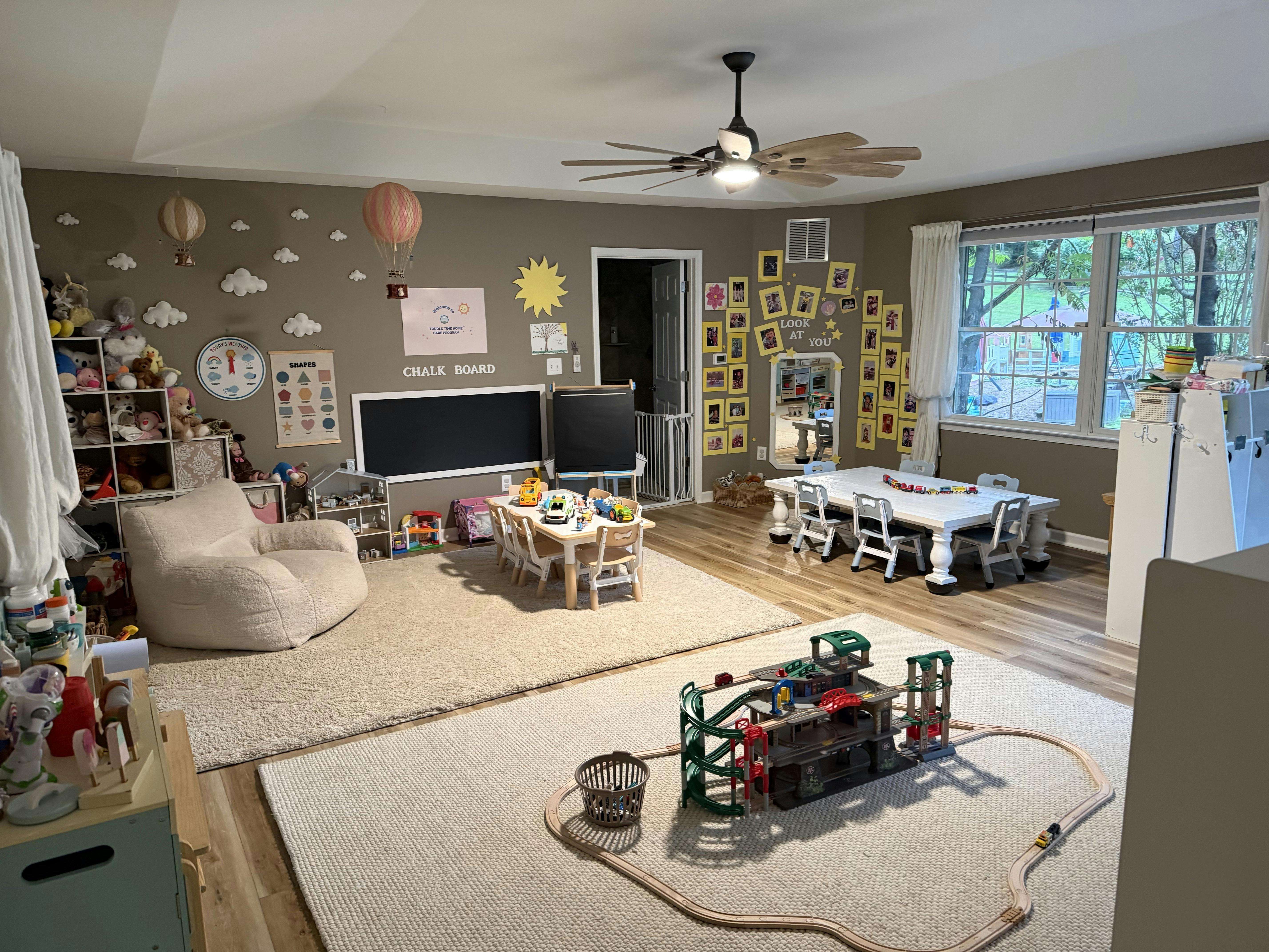 Spacious playroom with toy tables, rugs, and a wooden train set