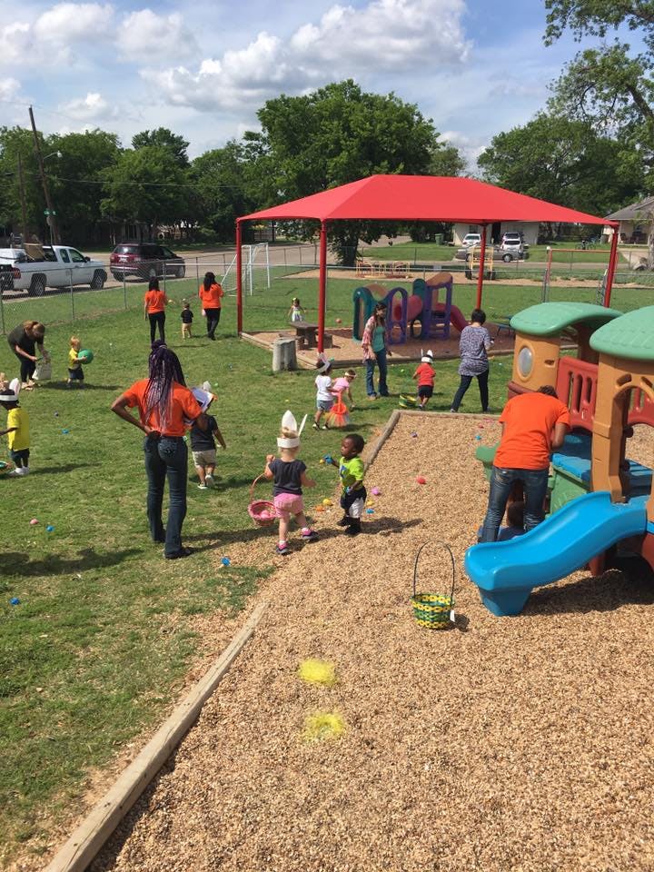People and children on a playground with a red canopy