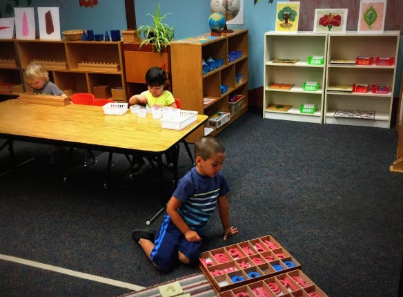 Three children playing with educational materials in a classroom